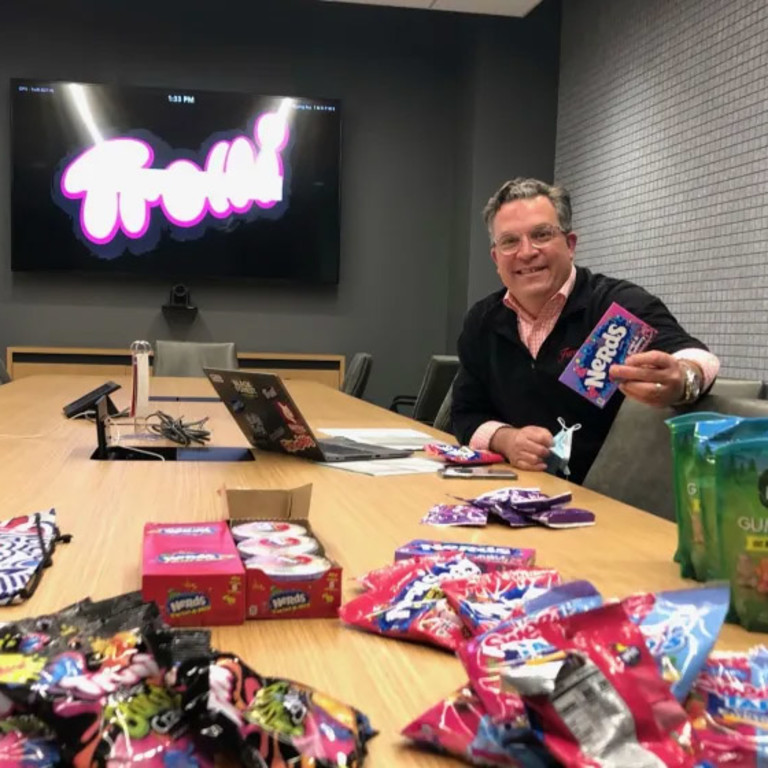 Greg Guidotti, Chief Marketing Officer smiling at the camera holding a box of Nerds